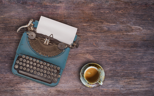 top view photo of vintage typewriter with blank page next to cup of coffee, on wooden table.