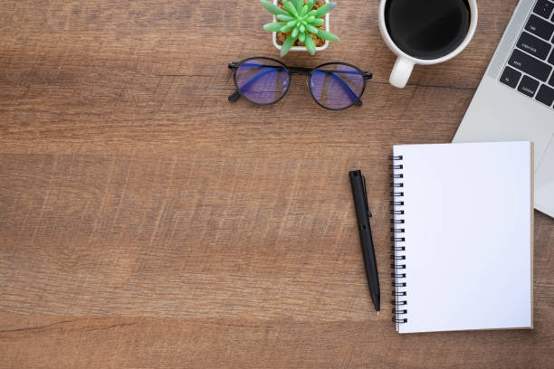 istock Top view above of Wooden office desk table with keyboard, notebook and coffee cup with equipment other office supplies. Business and finance concept. Workplace, Flat lay with blank copy space. 1282850127