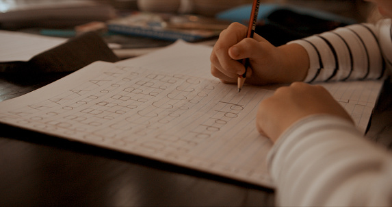 Closeup shot of a little girl writing letters of the alphabet in a book at home