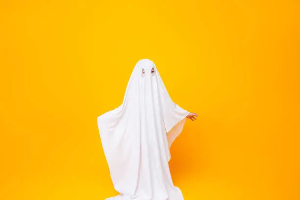 Little kid wearing cute halloween ghost costume on yellow background.