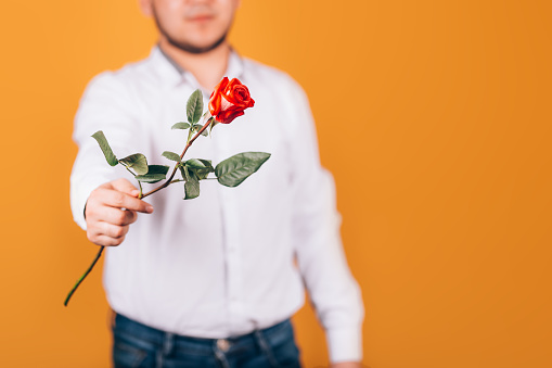 man holds a rose in his hand in a white shirt on an orange background