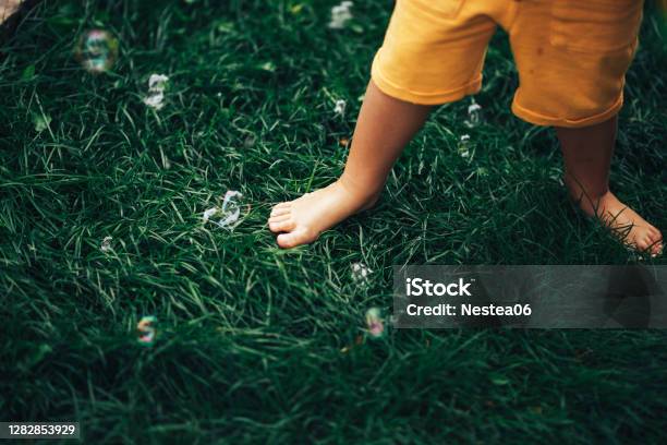 A Small Child Standing Barefoot On A Green Lawn A Child Tramples Soap Bubbles With His Feet Stock Photo - Download Image Now
