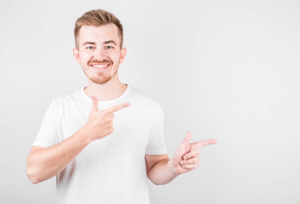 istock Look over there! Happy young handsome man in white shirt pointing away and smiling while standing against white background 1282855480