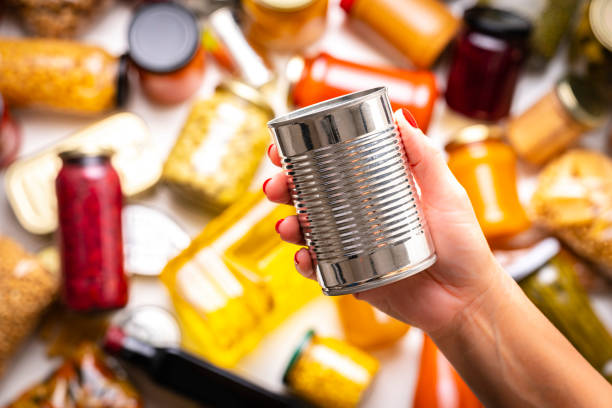 Female hand holding metal tin against defocused multicolored non-perishable food background. High resolution 42Mp studio digital capture taken with Sony A7rII and Sony FE 90mm f2.8 macro G OSS lens