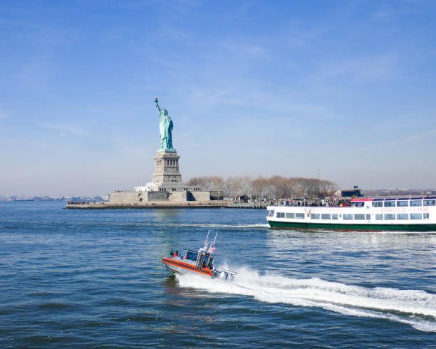 статуя свободы в нью-йоркской гавани с прицельным крейсером и гоночным оранжевым патрульным катером береговой охраны - usa coast guard ship nautical vessel стоковые фото и изображения