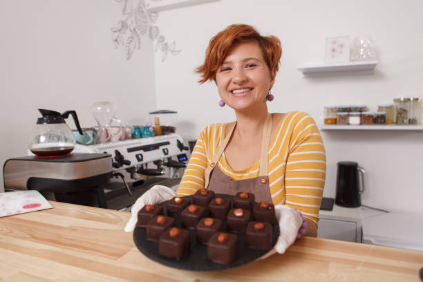 Female confectioner working at her cafe Selective focus on a tray full of delicious chocolate candy in the hands of happy female confectioner theobroma stock pictures, royalty-free photos & images