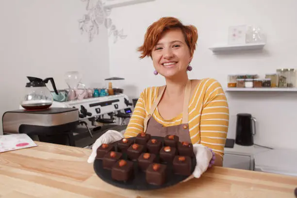 Selective focus on a tray full of delicious chocolate candy in the hands of happy female confectioner