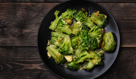 Top view of plate with roasted broccoli  on dark wooden table