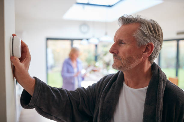 istock Mature Man Turning Control Dial On Digital Central Heating Thermostat At Home 1282867658
