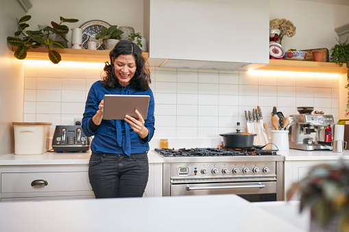 Mature Woman At Home In Kitchen Looking At Digital Tablet
