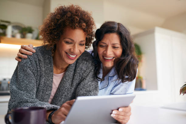 stesso sesso maturo coppia femminile a casa in cucina in pigiama bere caffè con tablet digitale - homosexual homosexual couple black ethnic foto e immagini stock