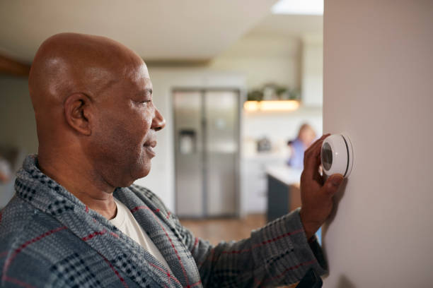 madura hombre girando el dial de control en el termostato de calefacción central digital en el hogar - termostato fotografías e imágenes de stock