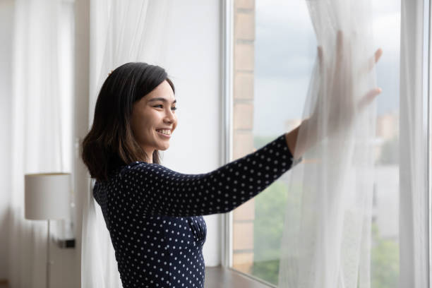 istock Smiling asian woman open curtains looking in distance 1282871836
