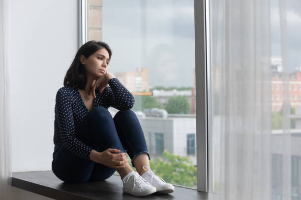 istock Unhappy asian woman sit on windowsill missing 1282871855