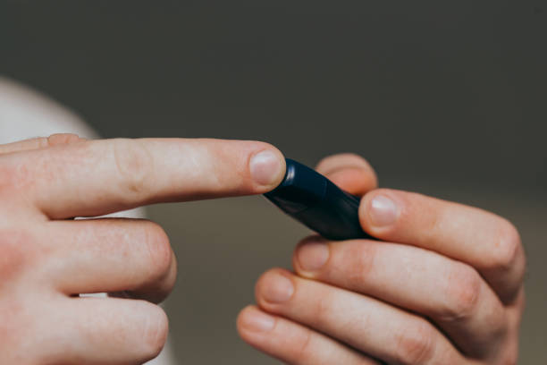 istock Close up of a man's hand using a lancet on his finger to check blood sugar using a glucose meter, using as medicine, diabetes, glycemia, healthcare and people concept. 1282874755