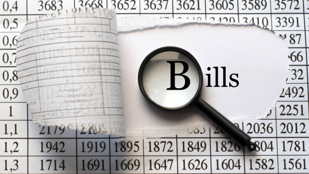 istock BILLS - word behind torn paper with numbers on a white background with a magnifying glass 1282874821