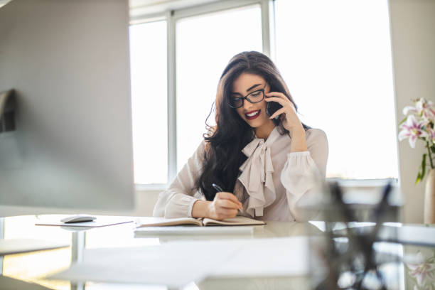 istock Portrait of beautiful young woman using her smart phone, reading documents and working in her office 1282880107