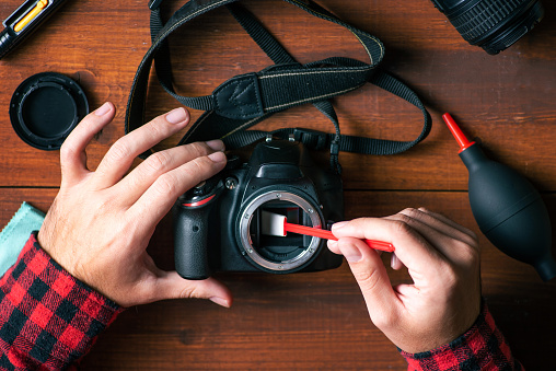 Man removing dust from a DSLR camera sensor with a cleaning stick close up