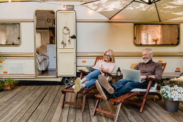 istock Pleased happy aged couple reading a book and using laptop while relaxing on the deck chairs near the camper van 1282880756