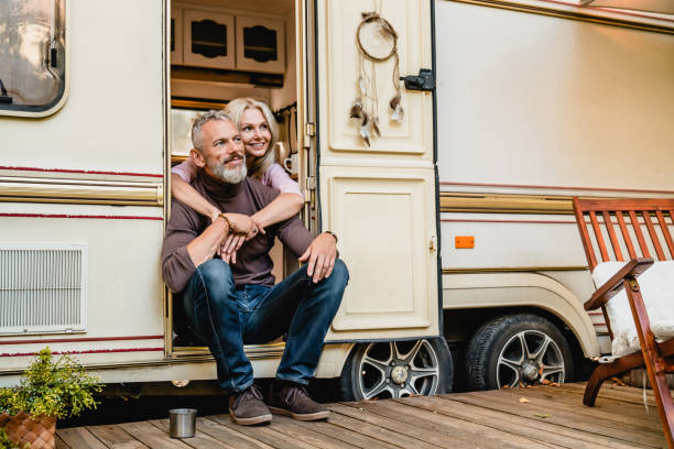 envejecida pareja feliz sentada en la puerta de la furgoneta y abrazada con amor - rv fotografías e imágenes de stock