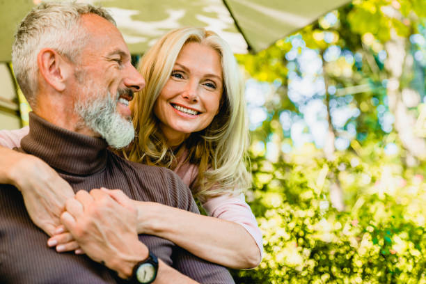 Beautiful aged blond woman hugging her grey-haired husband in park