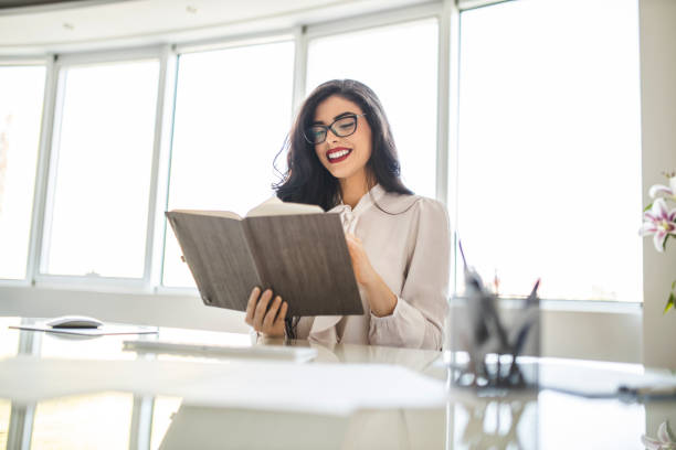 istock Young business woman reading diary, panning the day and working on computer in her office 1282881624