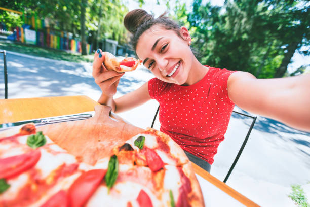 Teenage girl taking a selfie while eating pizza
