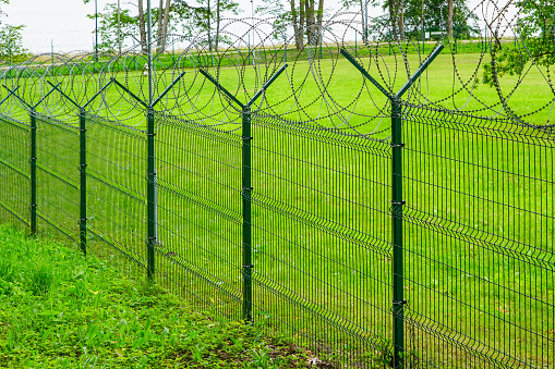 green metal fence with barbed wire around a military object