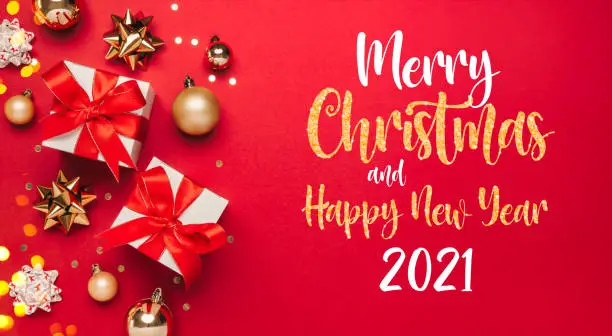 Photo of Merry Christmas and Happy New Year 2021 greeting card background with lettering. Christmas gifts and  golden decor on red background top view. Winter xmas holiday theme in flat lay