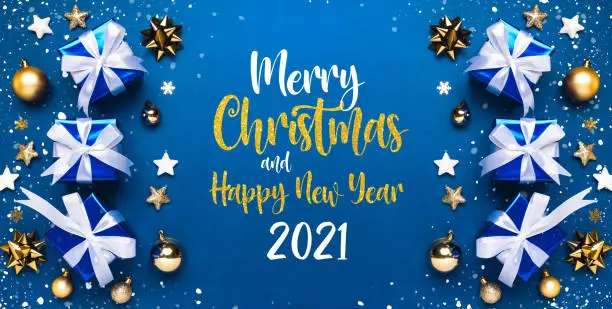 Photo of Merry Christmas and Happy New Year 2021 greeting card background with lettering. Christmas gifts and golden decor on blue background top view. Winter xmas holiday theme in flat lay