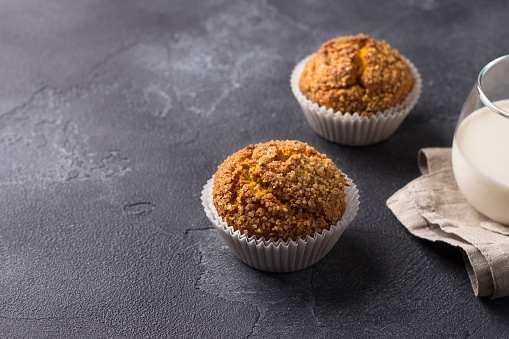 Delicious homemade pumpkin muffins with spicy sugar crust with milk on black textured background, space