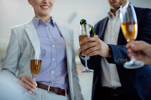 Close-up of businessman pouring Champagne in drinking glass while celebrating with coworkers in the office.