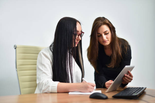 istock Two young female office workers use a tablet computer in a meeting 1282896906