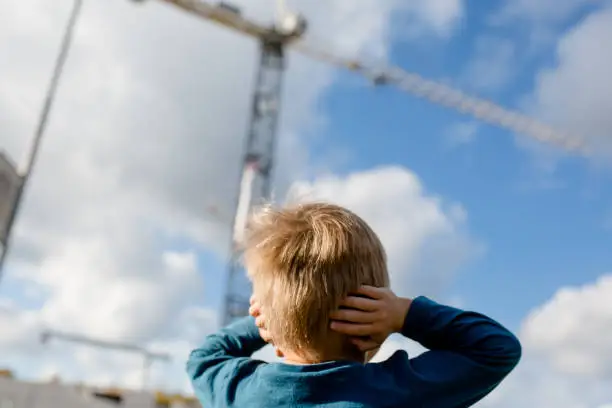 Toddler watches a crane and covers his ears with both hands