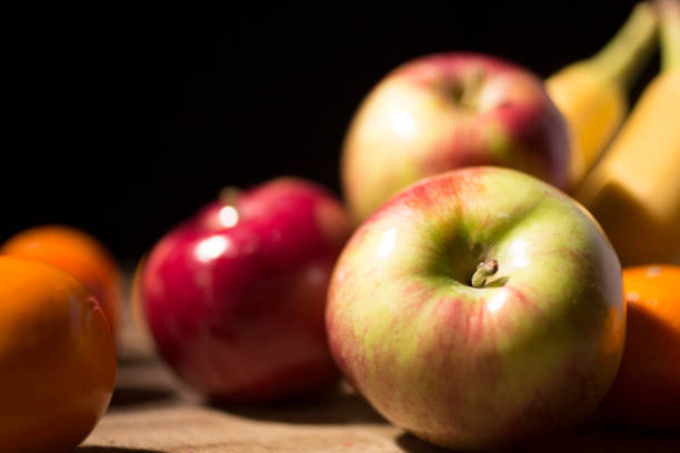 Display of fresh fruit, apples, oranges, bananas and tangerines.  Great space for your copy.  Black background with deep shadows to give an \