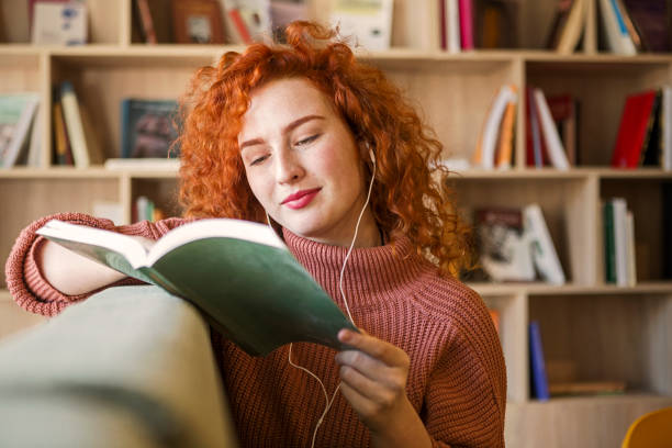 Happy young woman holding book reading wearing headphones Happy young woman holding book reading audio book stock pictures, royalty-free photos & images