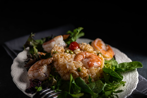 Shrimp risotto with peas and grape tomatoes served on mixed salad greens