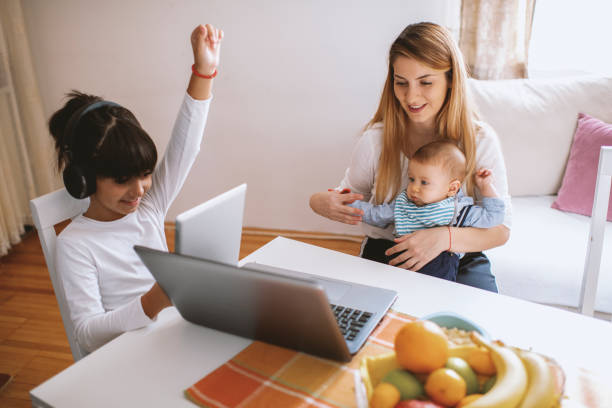 istock Mother working on laptop, holding baby boy and daughter learning on tablet 1282903652