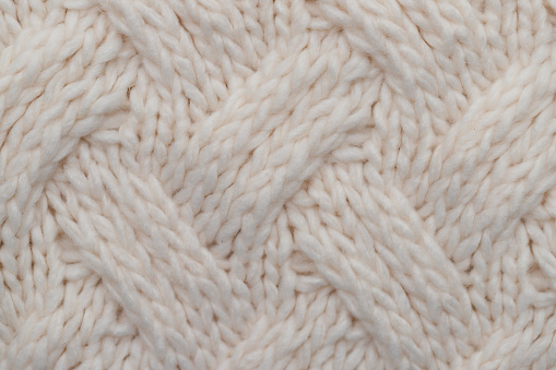Stack of knitted wool textile sweaters clothes on white blanket in bed at home room close up. Winter cozy season.