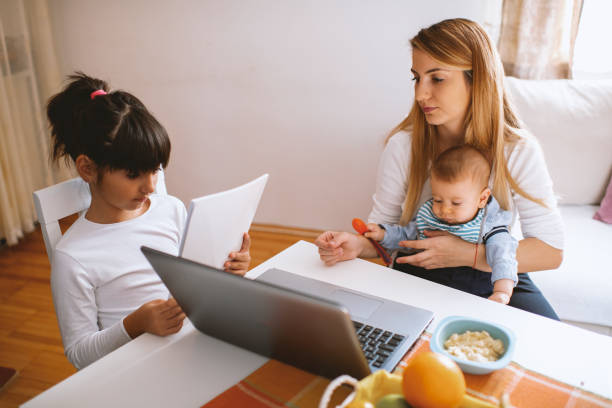 istock Mother working on laptop, holding baby boy and daughter learning 1282909536