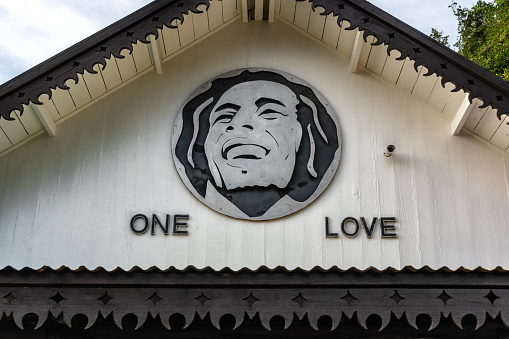 Nine Mile, Jamaica JANUARY 07, 2017: One Love is written and Bob Marley\s portrait at entry house to the Bob Marley Mausoleum compound. Building is partially obscured by beautiful flowers