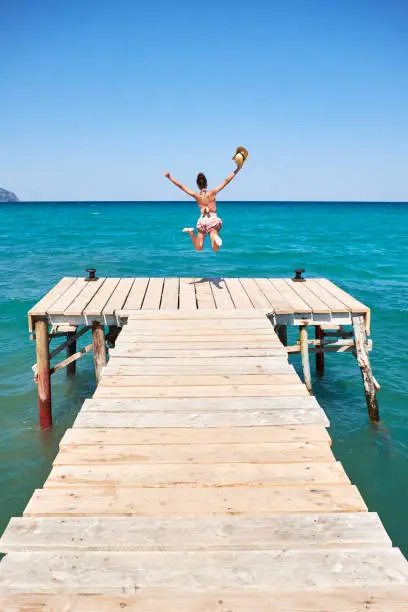 girl with hat jumping on a wooden wharf