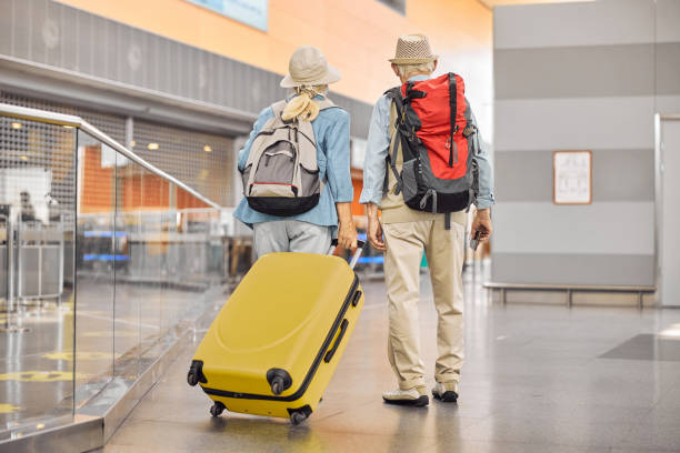 Two Caucasian elderly travelers standing at the airport Back view of a senior lady with a trolley suitcase and a man with a boarding pass boarding photos stock pictures, royalty-free photos & images