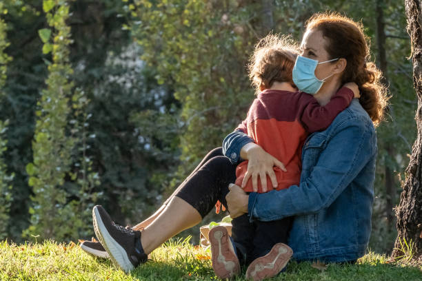 istock Mother and son embracing sitting in a park wearing protective face masks 1282916096