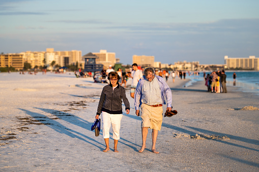 Sarasota, USA - April 28, 2018: Sunset sunny evening in Siesta Key, Florida with coastline coast ocean gulf of mexico on beach shore, senior couple walking
