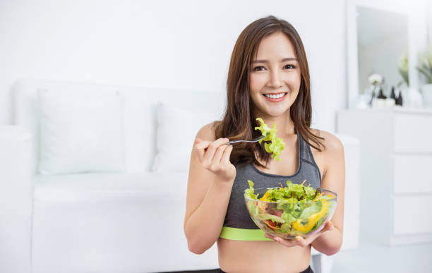 portrait of young beautiful asian girl in sportswear holding a glass bowl of salad fork in her hands. concept of vegan woman eating healthy food and tasty food health care medical plant base concept. - beautiful one person strength sensuality imagens e fotografias de stock