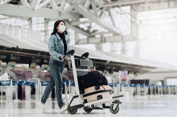 Asian tourist woman walking with luggage trolley Happy Asian tourist woman with mask protection for coronavirus walking with luggage trolley ready for travel asian tourist stock pictures, royalty-free photos & images