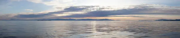 A beautiful panoramic sunset looking across Georgia Straight at Vancouver Island (Nanaimo) from the Sunshine Coast, British-Columbia on a calm day with pastel colours and clouds in the sky