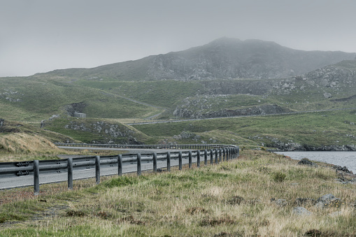 A road winds through the green hills of the Shetland Islands on a rainy autumn day.