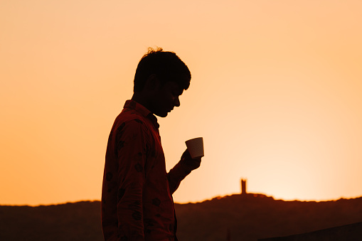 Silhouette of an Indian kid holding tea cup in front of the hill during the sunset